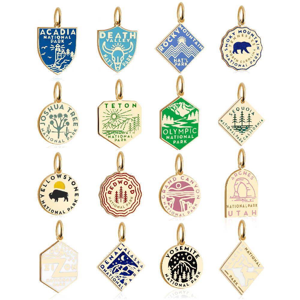 15 gold vermail and enamel National Park-themed charms with gold outlines, each representing a different park. The charms feature distinct colors and designs, including blue, green, yellow, red, purple, and pink. Shapes vary among shields, circles, hexagons, and diamonds, with graphics reflecting the unique aspects of each park, such as mountains, trees, and animals. Parks represented include Acadia, Death Valley, Rocky Mountain, Smoky Mountain, Joshua Tree, Teton, Olympic, Sequoia, Yellowstone, Redwood, Gr