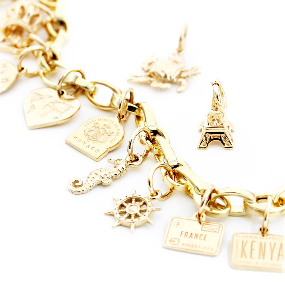 Solid 14k Gold Slim Infinity Link Charm Bracelet with a variety of solid gold travel charms from Jet Set Candy. Mini solid gold travel charms shown in this image include a solid gold France passport stamp charm, a 14k gold sea horse charm, a 14k gold Monaco souvenir charm, a solid gold ship’s wheel charm and a solid 14k gold mini Eiffel Tower charm. The bracelet and travel charms are all photographed on a white background. The bracelet is made in Italy.