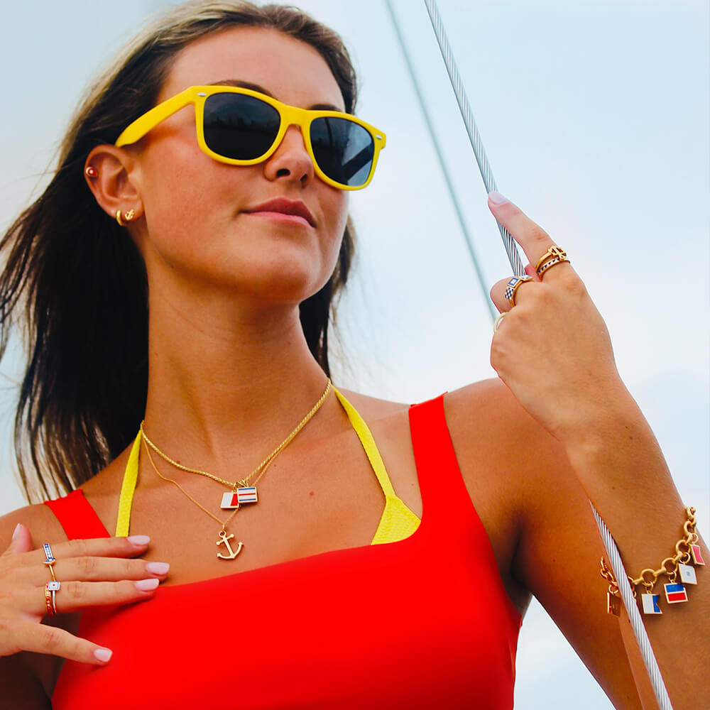 Gold charm necklace and bracelet featuring an anchor pendant and colorful Enamel charm flags in a nautical design.