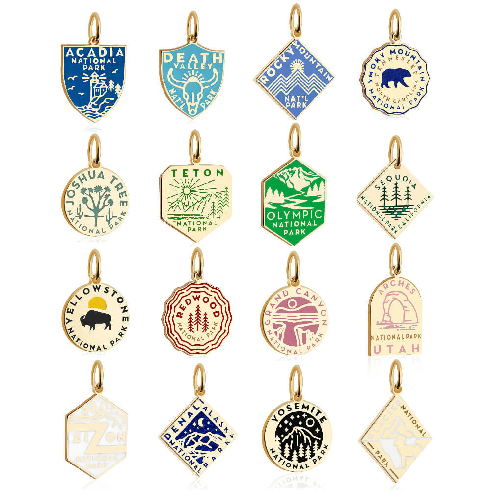 15 gold vermail and enamel National Park-themed charms with gold outlines, each representing a different park. The charms feature distinct colors and designs, including blue, green, yellow, red, purple, and pink. Shapes vary among shields, circles, hexagons, and diamonds, with graphics reflecting the unique aspects of each park, such as mountains, trees, and animals. Parks represented include Acadia, Death Valley, Rocky Mountain, Smoky Mountain, Joshua Tree, Teton, Olympic, Sequoia, Yellowstone, Redwood, Gr