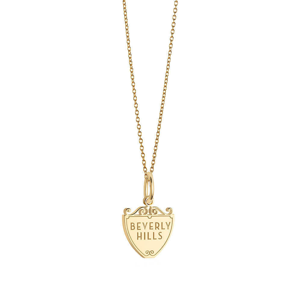 Gold charm featuring Beverly Hills engraving on a shield shape with scrollwork accents and a matching cable chain.