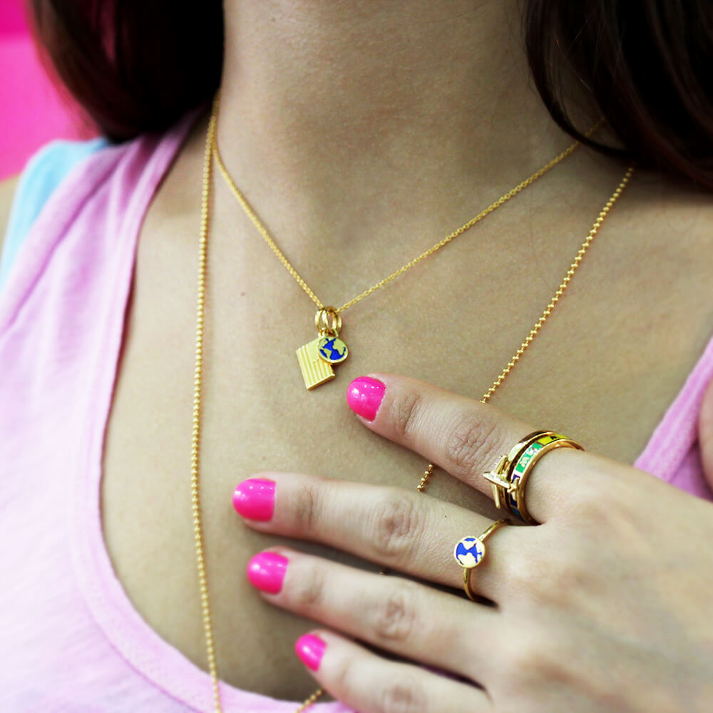 Gold mini globe charm necklace and ring by Jet Set Candy, featuring detailed enamel globe designs, worn by a model.