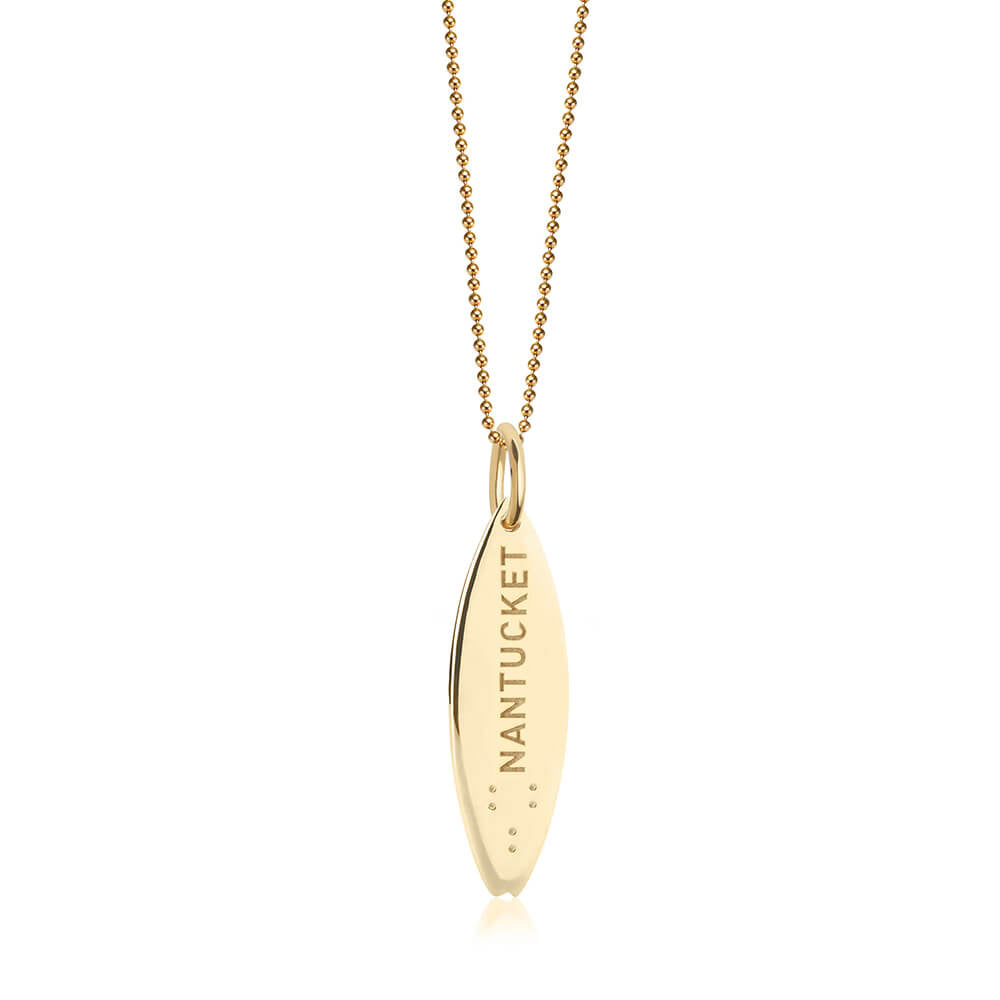 Gold surfboard charm featuring Nantucket engraving and Braille dots, hanging from a gold bead chain necklace with polished finish.