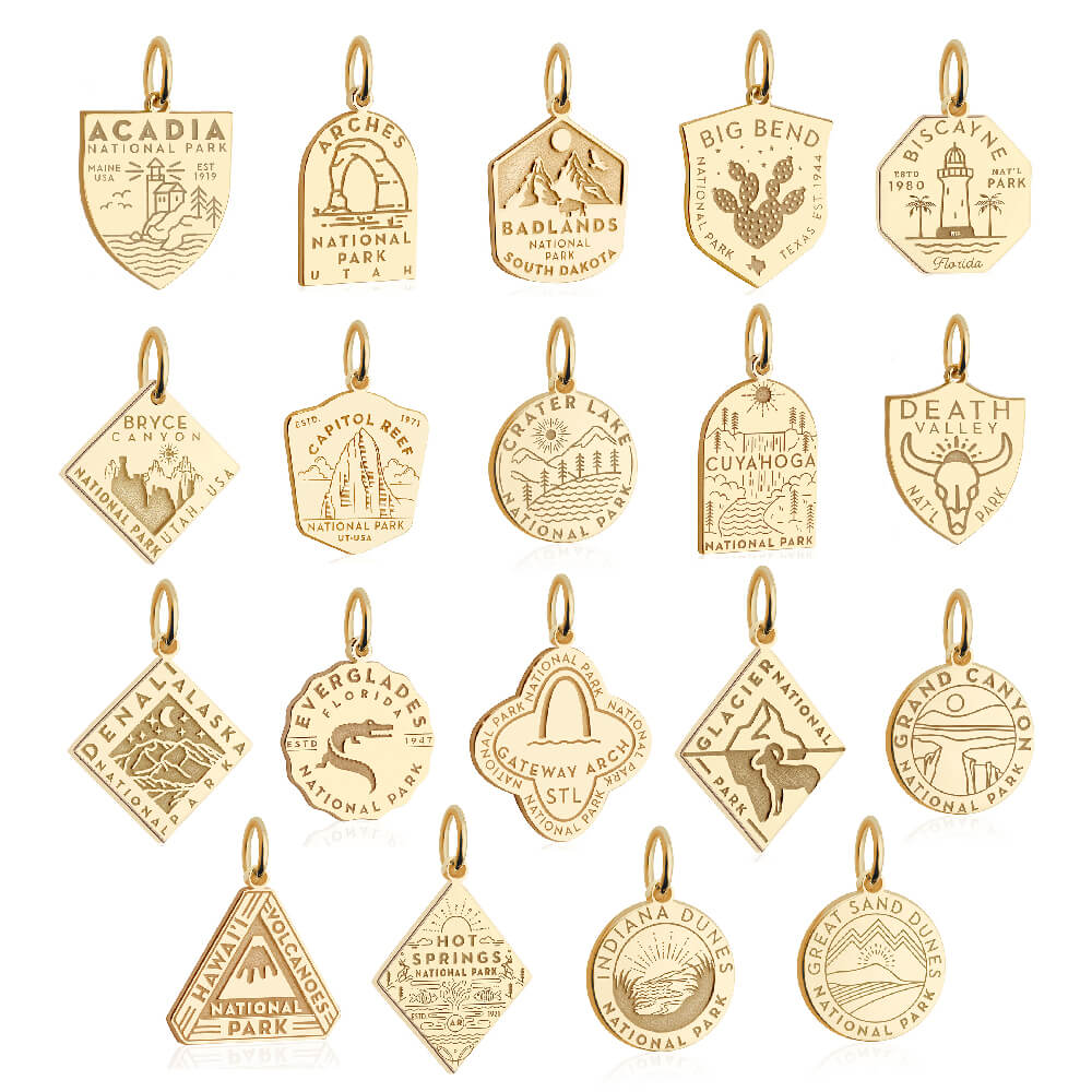 Collection of 18 gold charms, each representing a different U.S. national park. Each charm has a polished gold border, a small loop for attachment, and features detailed illustrations and inscriptions specific to the park, such as Acadia, Arches, Badlands, Big Bend, Biscayne, Bryce Canyon, Capitol Reef, Crater Lake, Cuyahoga Valley, Death Valley, Denali, Everglades, Gateway Arch, Glacier, Grand Canyon, Hawaii Volcanoes, Hot Springs, and Indiana Dunes. iconic landmarks