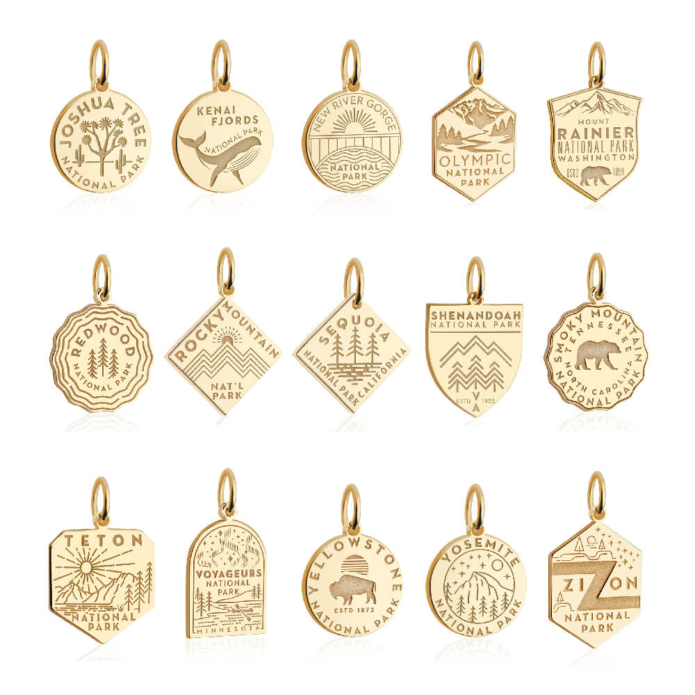 15 gold vermeil National Park-themed charms, each representing a different park. The charms are arranged in three rows of five. Each charm has unique engraved designs and shapes, including shields, circles, hexagons, and diamonds. Parks represented include Joshua Tree, Kenai Fjords, New River Gorge, Olympic, Mount Rainier, Redwood, Rocky Mountain, Sequoia, Shenandoah, Smoky Mountain, Teton, Voyageurs, Yellowstone, Yosemite, and Zion.