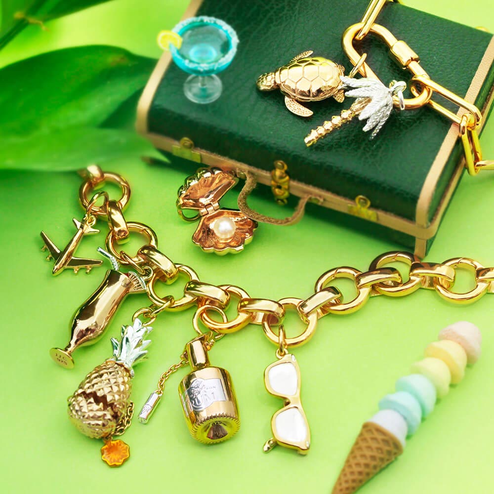 Two-Tone and Gold charm collection featuring an airplane, pineapple, sea turtle, palm tree, pearl shell, and cocktail motifs.