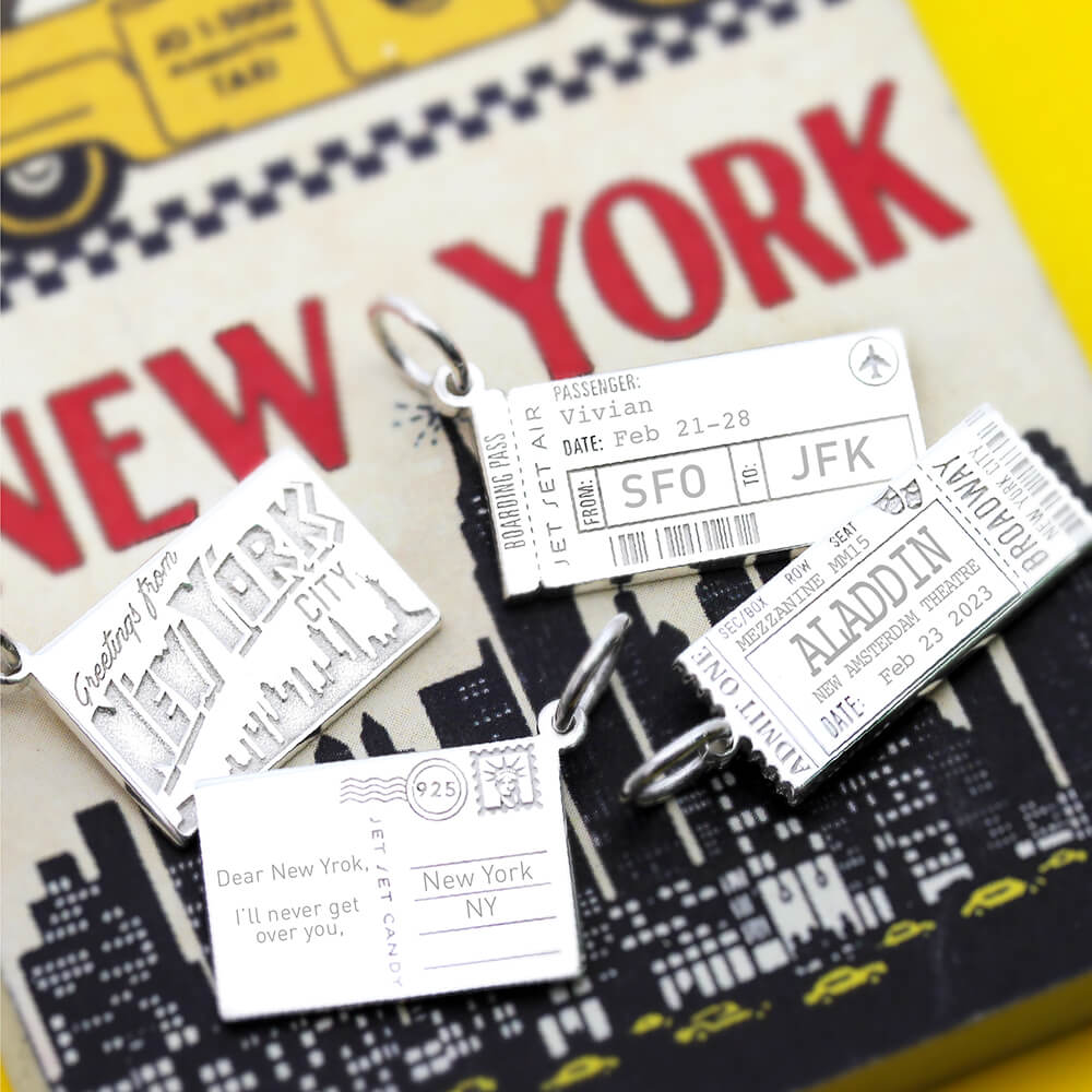 Sterling Silver charms featuring a New York postcard, Aladdin Broadway ticket, boarding pass with SFO to JFK, and skyline.