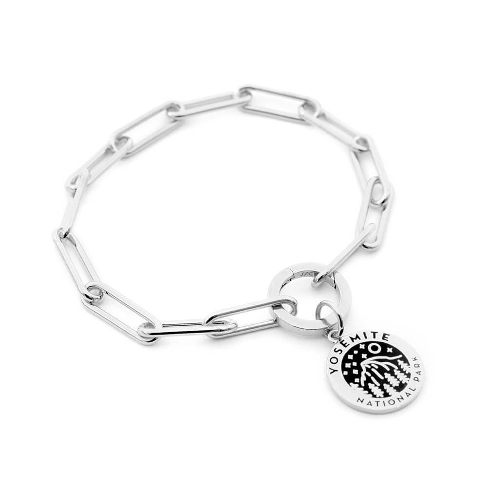 The image shows a sterling silver 360 daily bracelet, a paperclip chain bracelet featuring a charm representing Yosemite National Park. The charm is round with a black enamel design of a landscape and starry sky, along with the text 