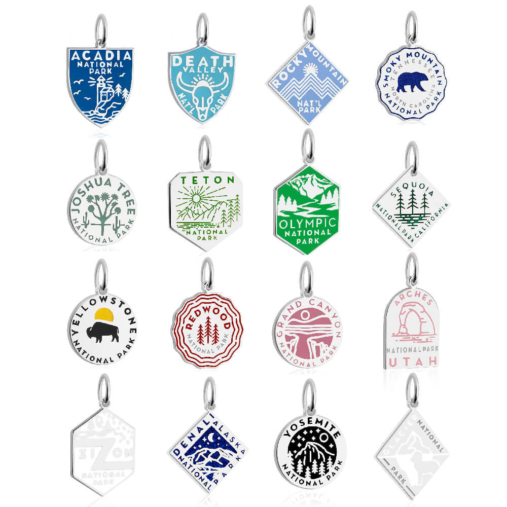15 sterling silver and enamel National Park-themed charms, each representing a different park. The charms feature distinct colors and designs, including blue, green, yellow, red, purple, and pink. Shapes vary among shields, circles, hexagons, and diamonds, with graphics reflecting the unique aspects of each park, such as mountains, trees, and animals. Parks represented include Acadia, Death Valley, Rocky Mountain, Smoky Mountain, Joshua Tree, Teton, Olympic, Sequoia, Yellowstone, Redwood, Grand canyon, arch