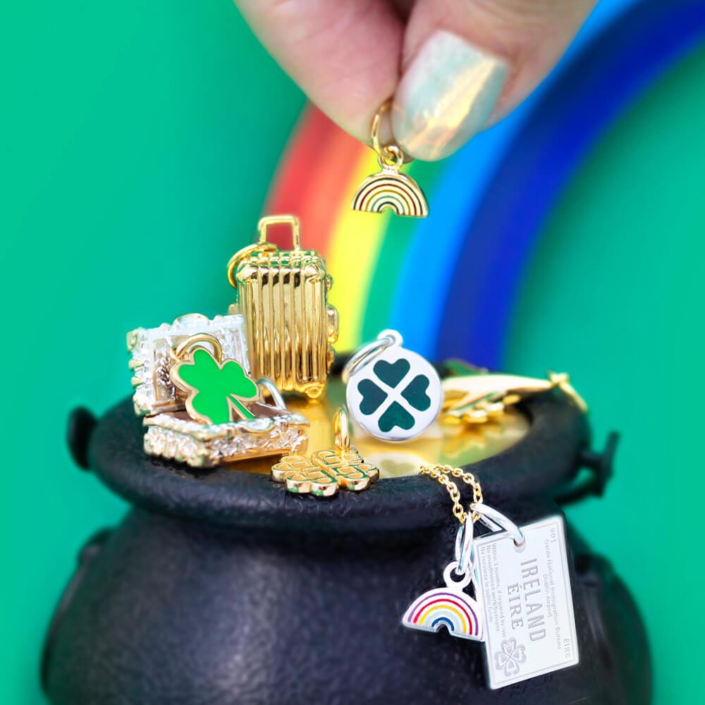Two-Tone charms featuring a gold suitcase, green enamel shamrock, sterling silver Ireland passport tag, and rainbow motifs on a cauldron.