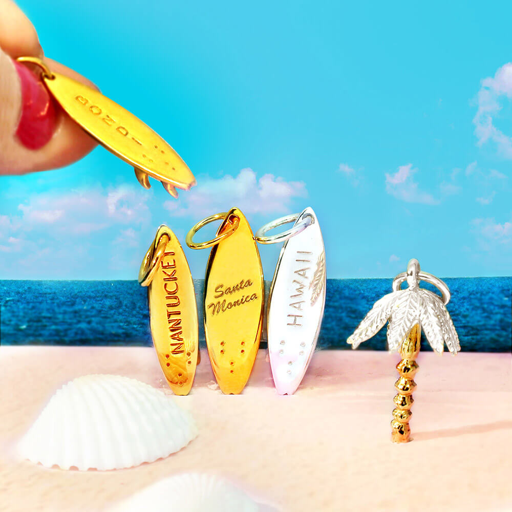 Gold and Sterling Silver surfboard charms with Bondi, Nantucket, Santa Monica, and Hawaii engravings and a Two-Tone palm tree.