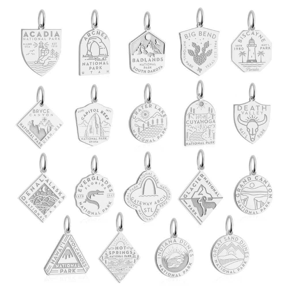 20 silver-toned National Park-themed charms, each representing a different park with engraved designs. The charms are arranged in a grid of four rows and five columns, featuring parks like Acadia, Arches, Badlands, Big Bend, Biscayne, Bryce Canyon, Capitol Reef, Crater Lake, Cuyahoga Valley, Death Valley, Denali, Everglades, Gateway Arch, Glacier, Grand Canyon, Hawaii Volcanoes, Hot Springs, Indiana Dunes, and Great Sand Dunes mountains, trees, and landmarks