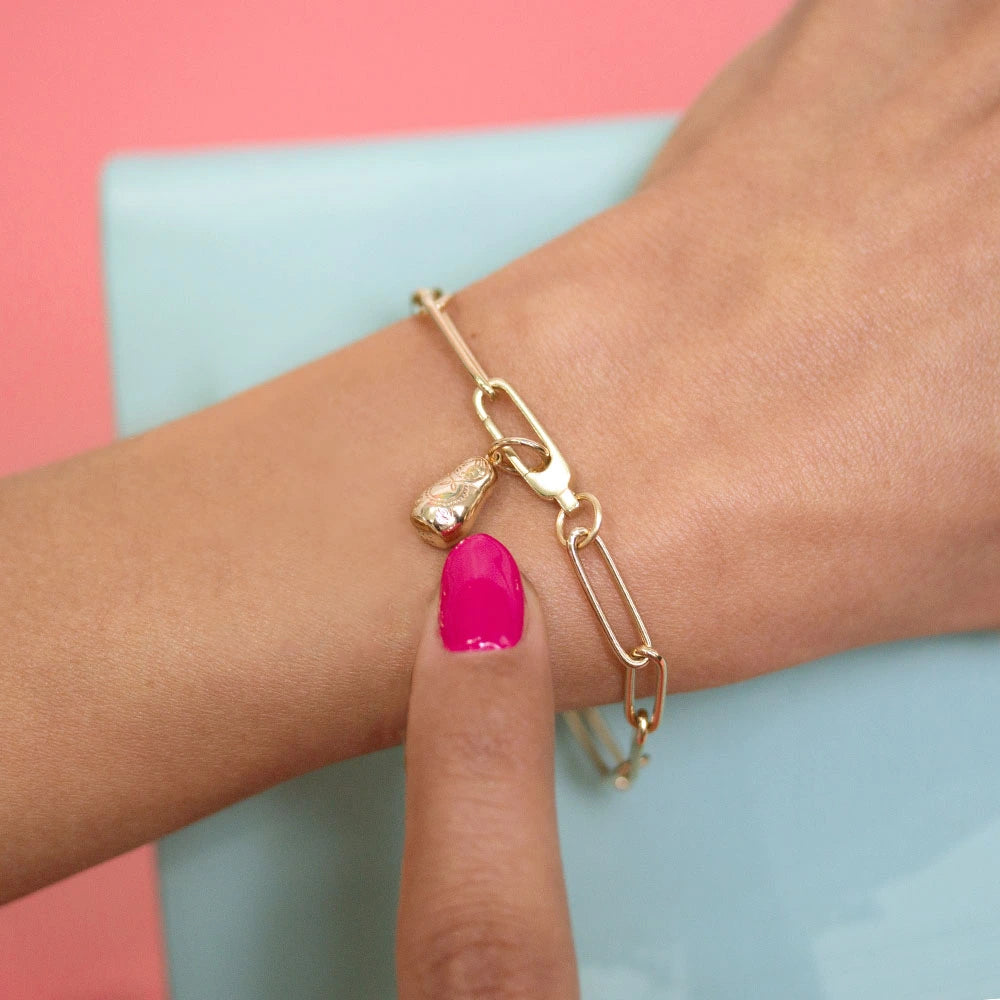 Gold charm in the shape of a 3D Russian nesting doll featuring detailed engravings on a paperclip chain bracelet.
