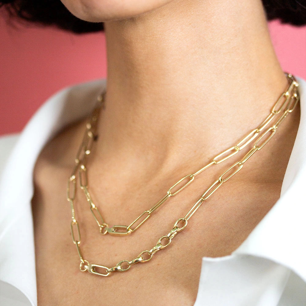 Gold layered paperclip chain necklace set featuring elongated rectangular links and polished finish worn on a person's neck.