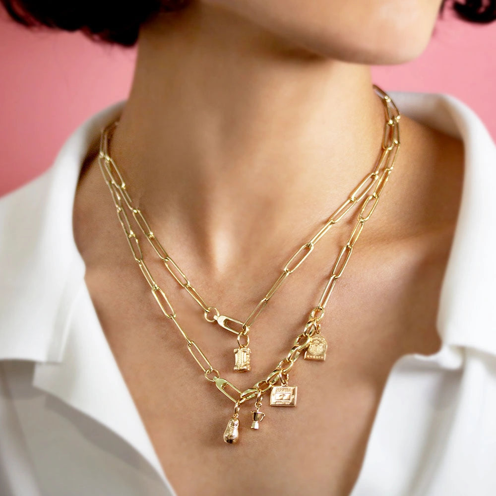 Gold Charm paperclip necklaces featuring a 3D moka pot, luggage tag, and travel stamp charms with detailed engravings.
