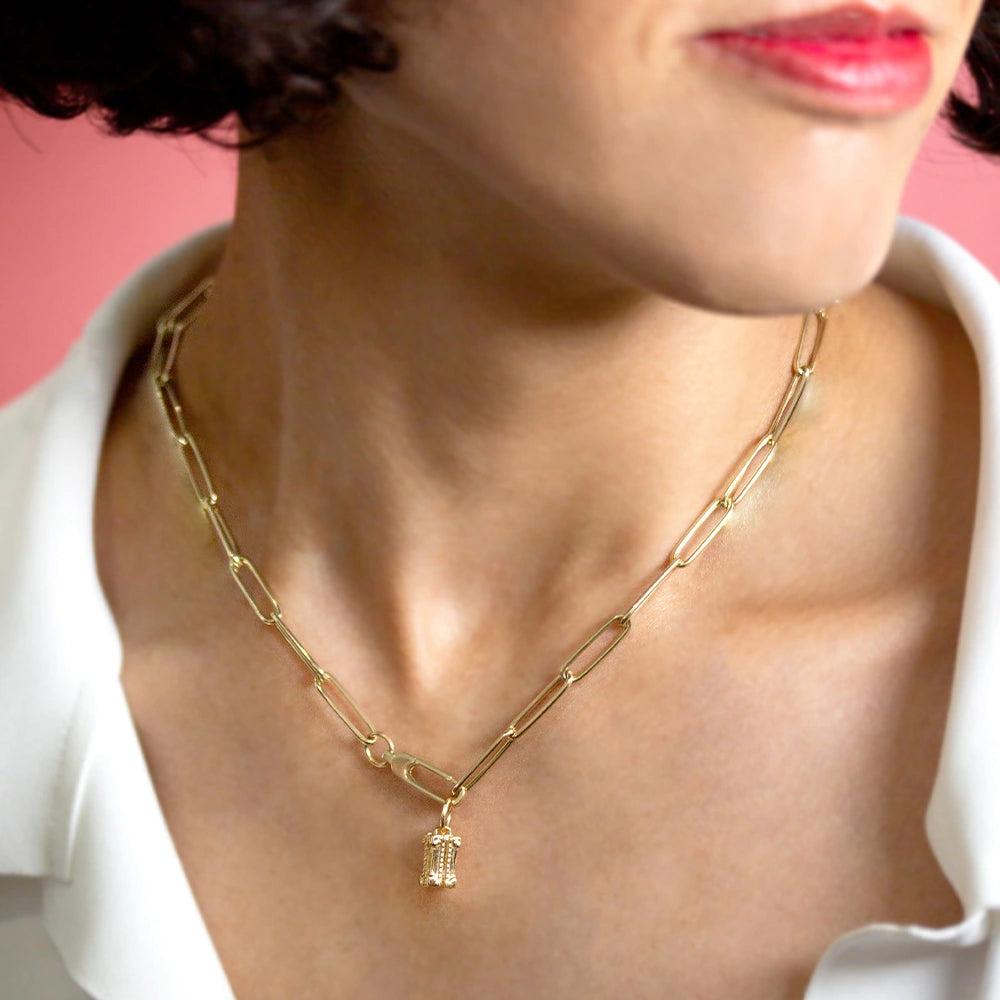 Gold Charm in a detailed 3D column shape hanging from a gold paperclip link chain on a woman.