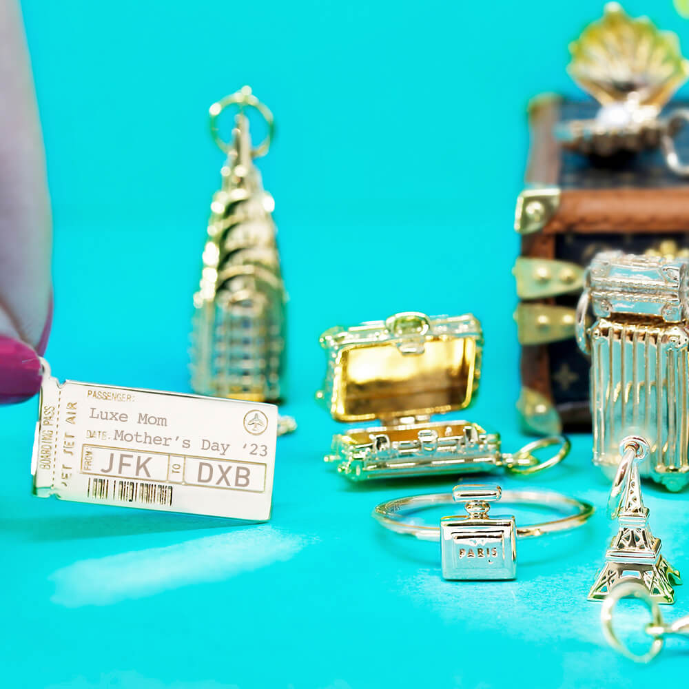Gold boarding pass charm featuring JFK to DXB engravings, Luxe Mom text, airplane icon, and Mother's Day '23 date.