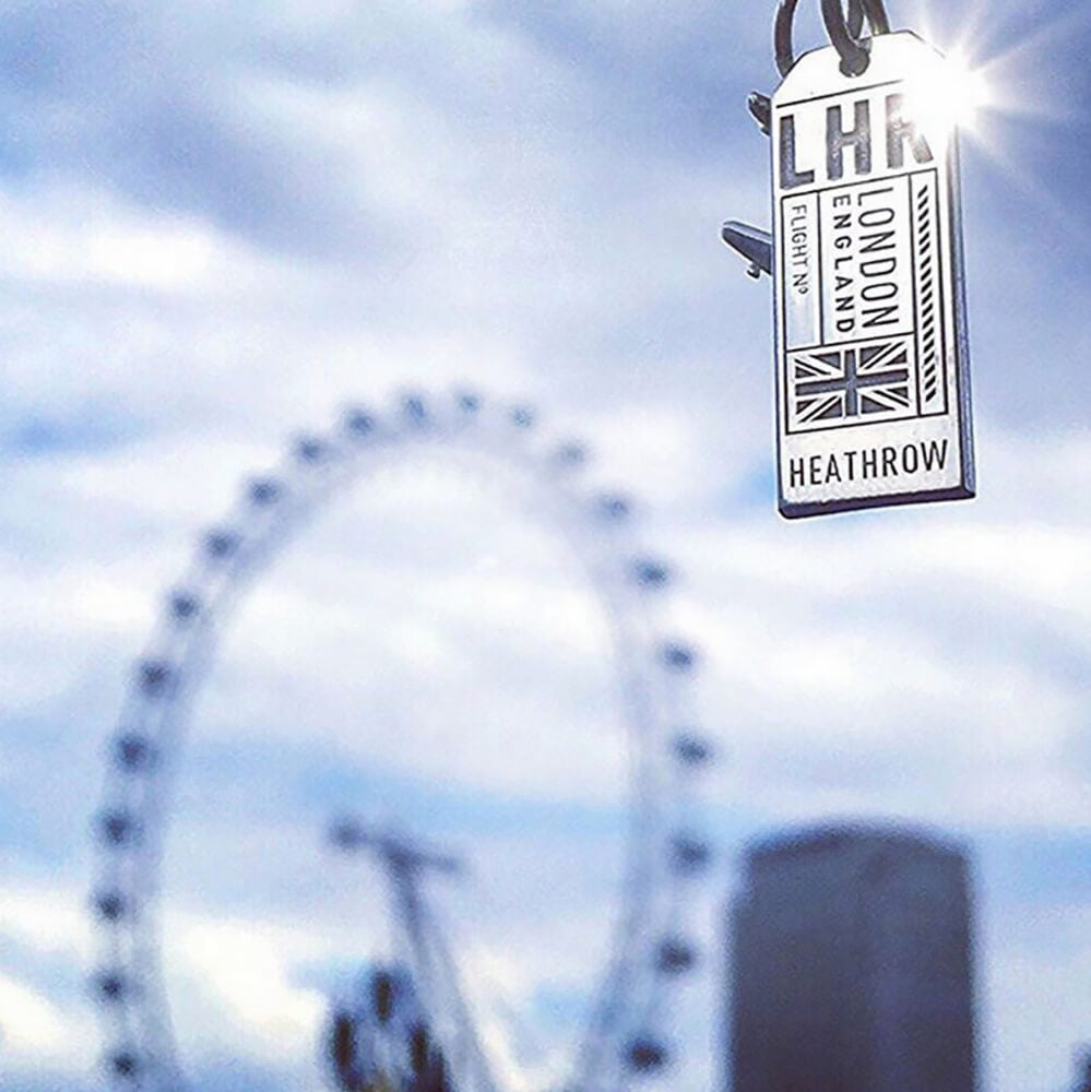 Sterling Silver LHR London England Luggage Tag Charm from JET SET CANDY photographed in front of the London Eye on a blue cloudy sky