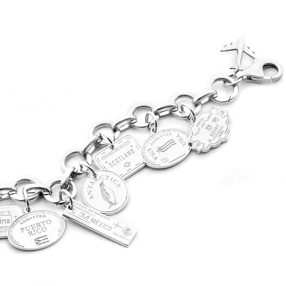 Sterling SIlver Travel Charm Bracelet featuring Passport Stamp Charms from Jet Set Candy. The bracelet includes a Puerto Rico Passport Stamp Charm, a Mexico Passport Stamp Charm, an Antarctica Passport Stamp Charm, a Scotland Passport Stamp Charm, a USA Passport Stamp Charm, and an Egypt Passport Stamp Charm all from Jet Set Candy. The bracelet also features a plane charm and is on a white backdrop. 