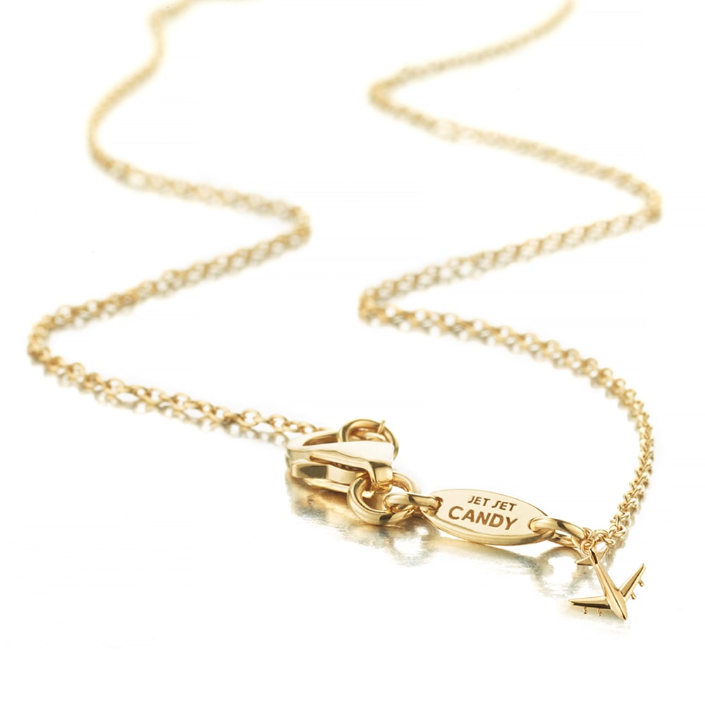Gold vermeil cable chain shown in a snaking position on a white background with a focus on the small branded back tag that has “Jet Set Candy” engraved into and next to their tiny signature airplane charm that hangs next to the tag near the clasp at the back of the chain.