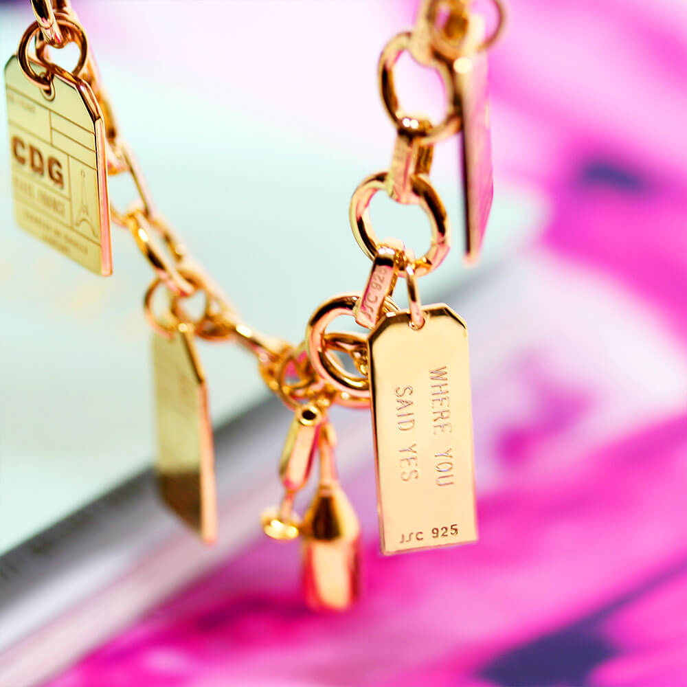 Gold Infinity Link Charm Bracelet from Jet Set Candy showing the back of a luggage tag charm engraved with 