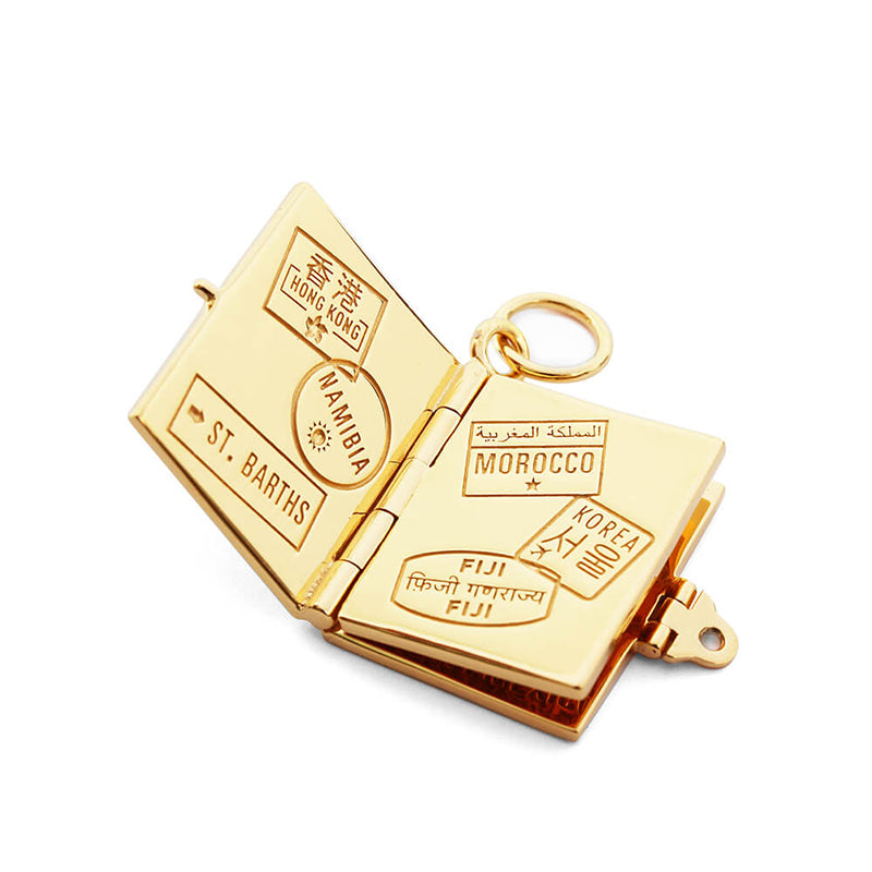 Bespoke Solid 14k Gold USA Passport Book Charm shown open to a spread of solid gold pages inside, sitting on a white background. This charm is fully customizable and you can choose up to 12 passport stamps to include on the solid gold pages inside. Shown in this photo are passport stamps for St. Barths, Namibia, Hong Kong, Morocco, Fiji, and Korea. This charm is a one-of-a-kind souvenir.