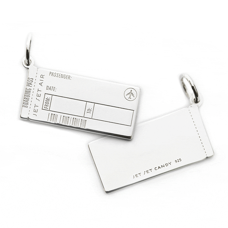 Animated GIF of a Sterling Silver Boarding Pass Charm from JET SET CANDY shown on a white background. The customizable engraving is being animated. On the front, the engraving shows “Amal + George” and the airport codes VCE and LHR being added the back is shown being engraved with “La Dolce Vita.” The charm looks very similar to a real boarding pass and includes an airplane icon and fake engraved bar code.