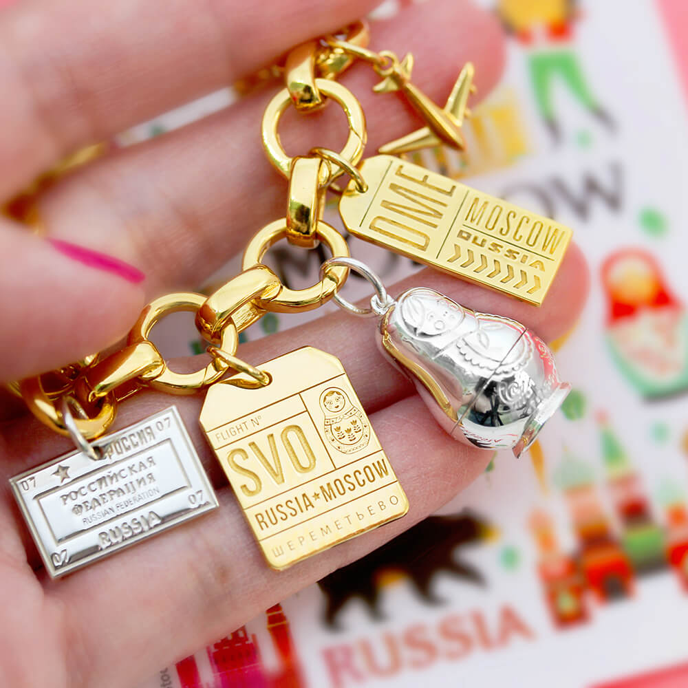 Sterling silver Russian nesting charm with Russian luggage tag charms featured on a gold link bracelet by Jet Set Candy.
