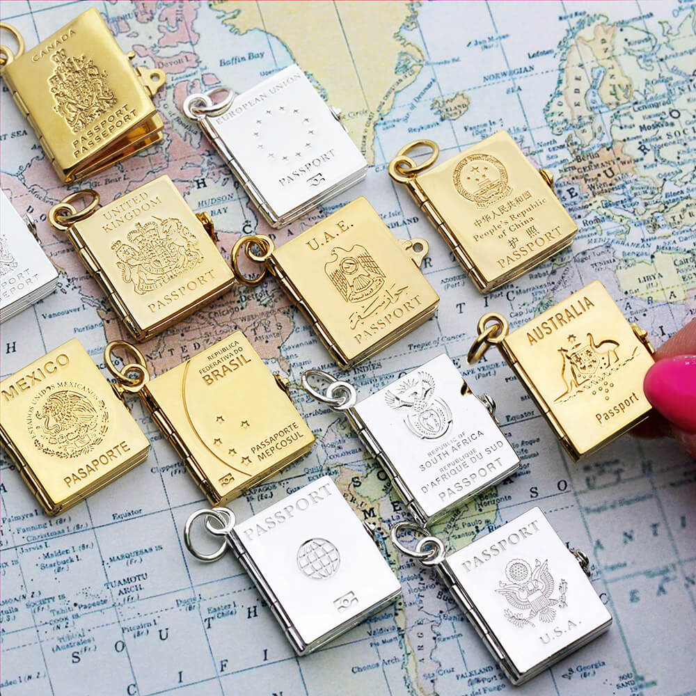 Silver and gold passport book charms by Jet Set Candy, displayed together on a map background.