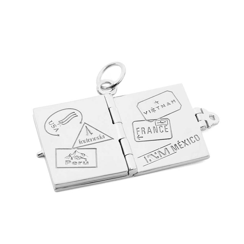 Silver passport book charm by Jet Set Candy, with interior stamp engravings representing international travel on a white background.