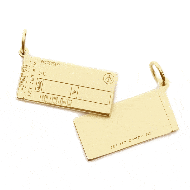 Animated GIF of a sold gold Boarding Pass Charm from Jet Set Candy shown on a white background. The customizable engraving is being animated. On the front, the engraving shows “Amal + George” and the airport codes VCE and LHR being added the back is shown being engraved with “La Dolce Vita.” The charm looks very similar to a real boarding pass and includes an airplane icon and fake engraved bar code.